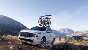 A white 2022 Hyundai Santa Fe being driven with two bikes on the roof in an  open field with mountains in the background. | Hyundai dealer in North Little Rock, AR.
