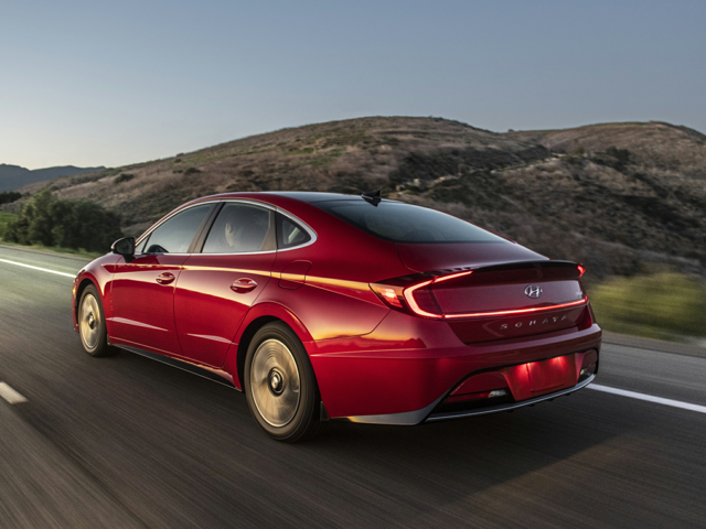 Rear angle view of a red 2023 Hyundai Sonata Hybrid driving along a scenic highway at sunset